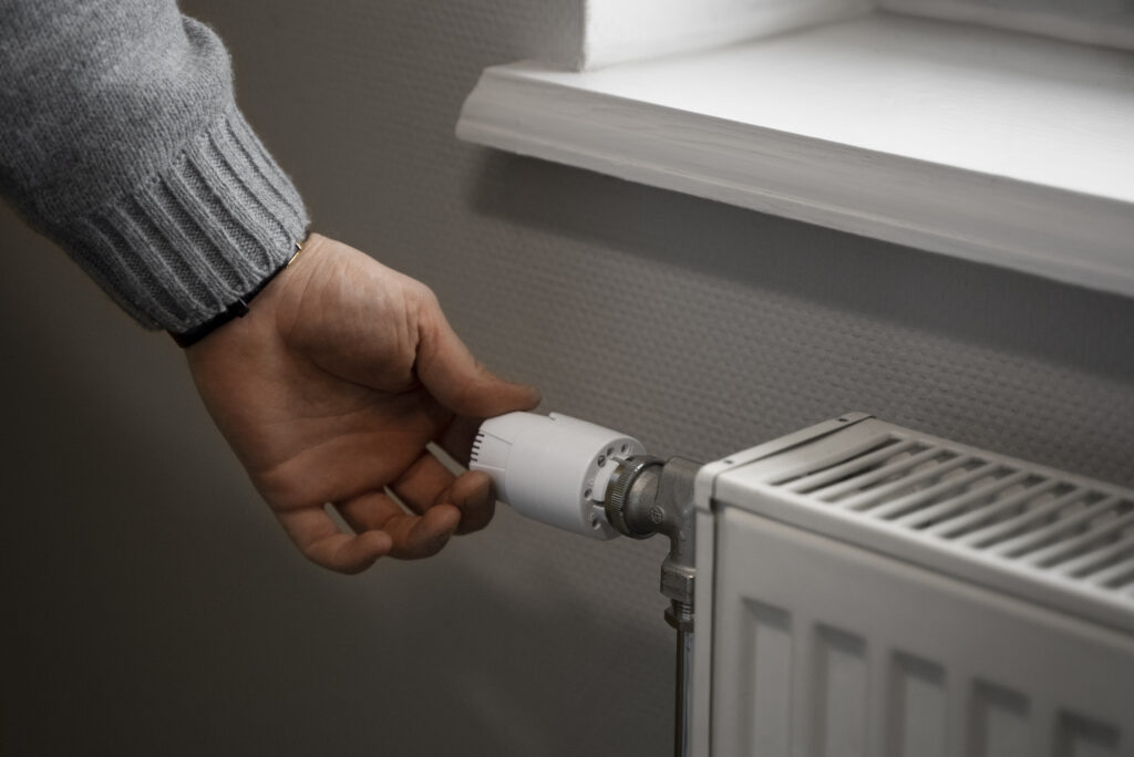 A man turning down the thermostat on a radiator to save on his propane bill